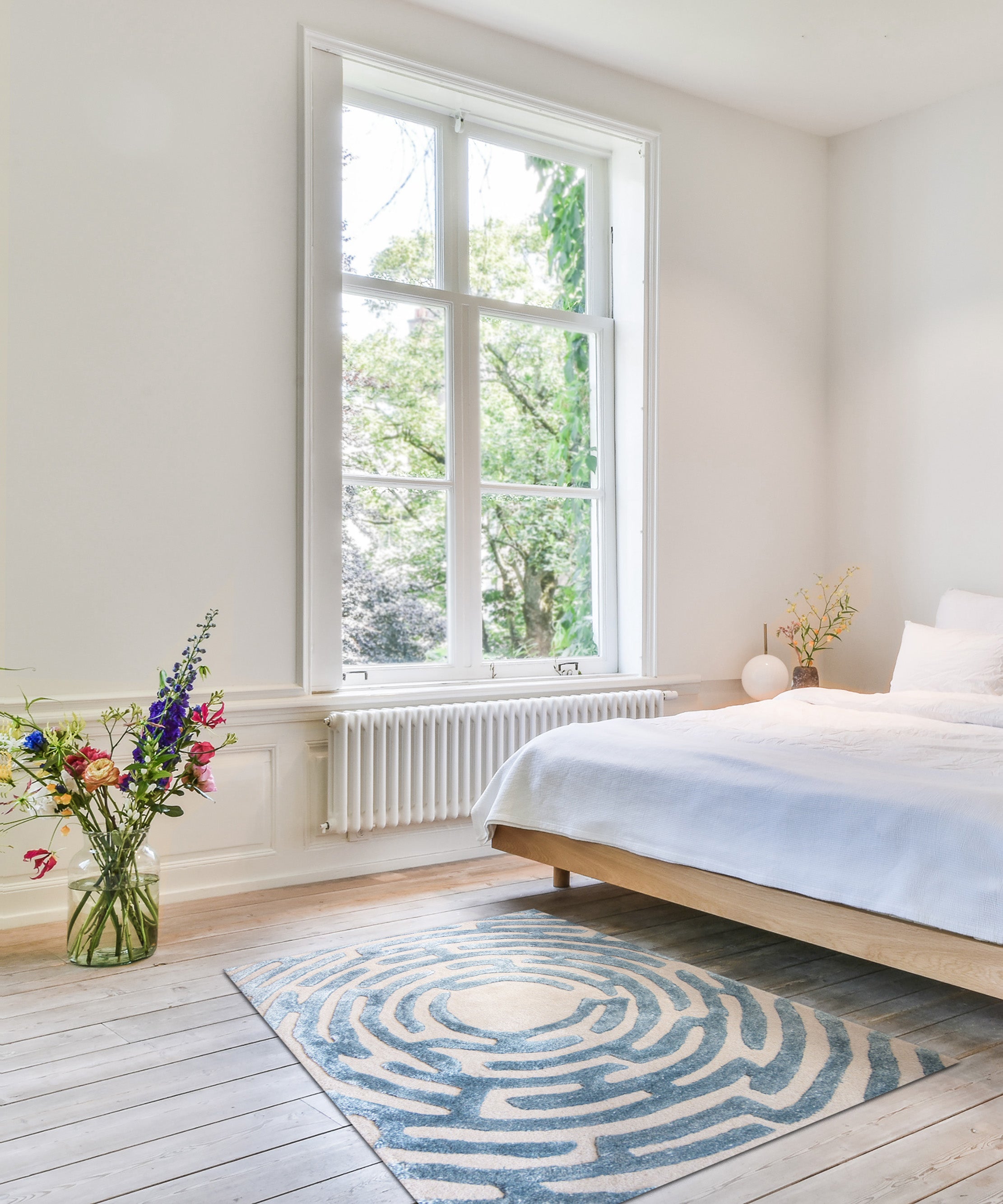 A bedroom with a sky blue Maze luxury floor rug at the end of the bed 