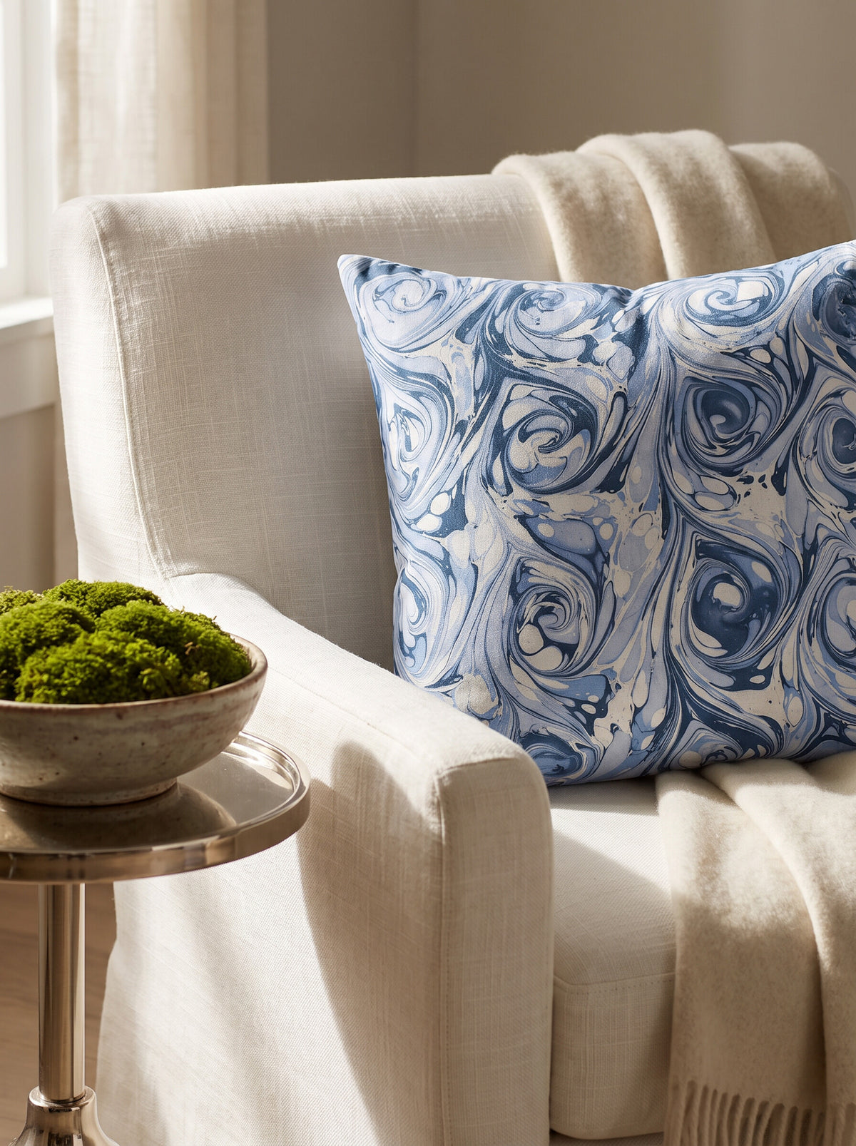 The Andrews hand-marbled pillow cover in blue and white styled on a cream linen armchair
