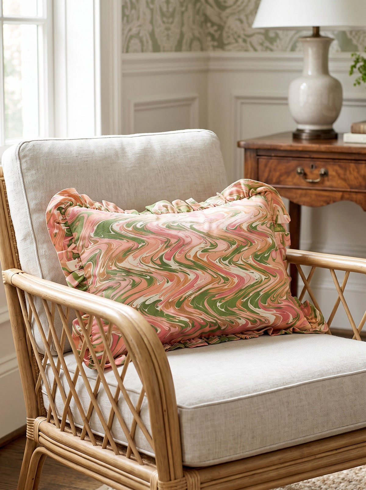 The Arden ruffled hand-marbled lumbar pillow cover in pink and green styled on a rattan armchair