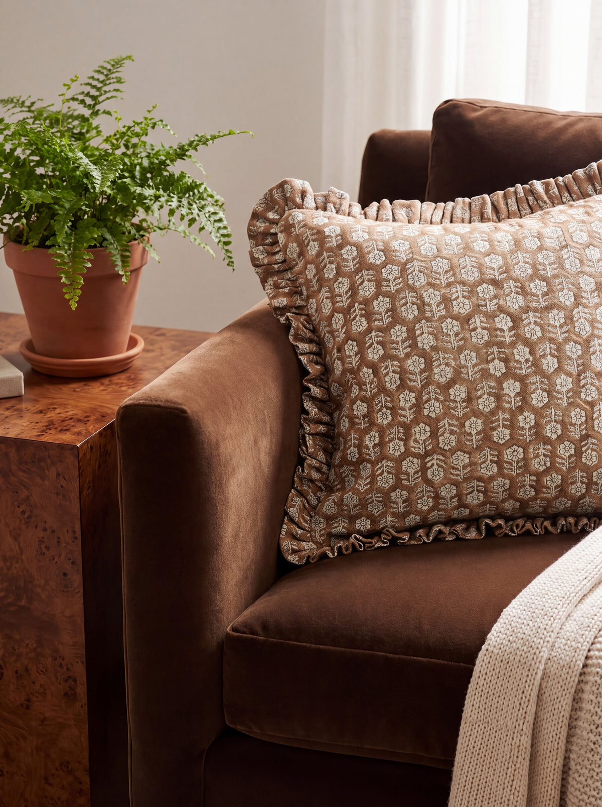The Austell ruffled block print pillow cover styled on a brown velvet sofa beside a burl side table