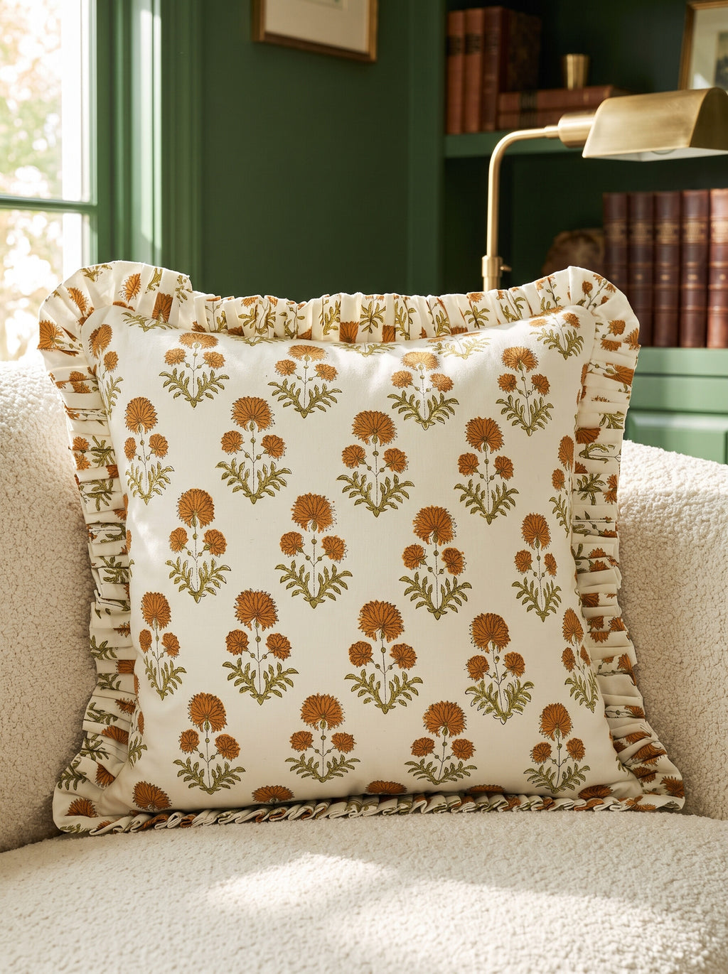 The Collier ruffled block print pillow cover in mustard and green styled on a cream boucle chair in a green library