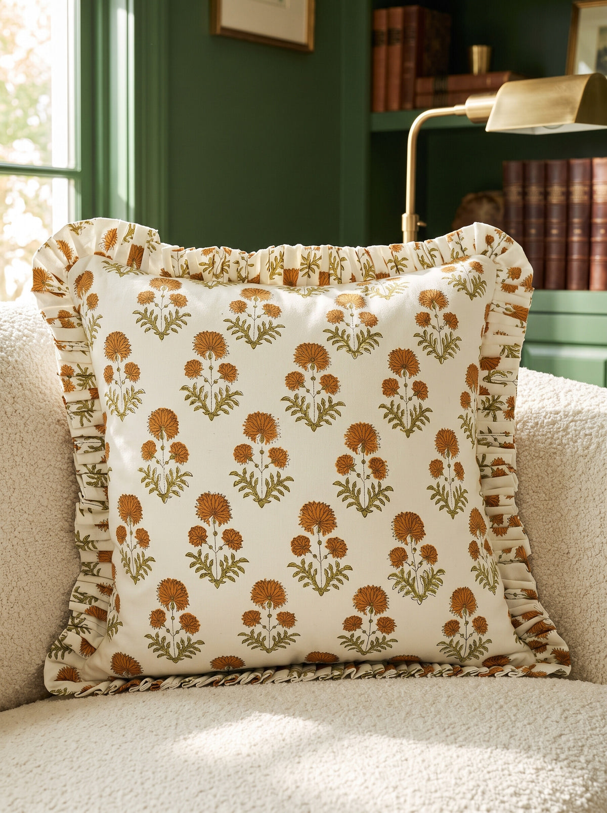 The Collier ruffled block print pillow cover in mustard and green styled on a cream boucle chair in a green library