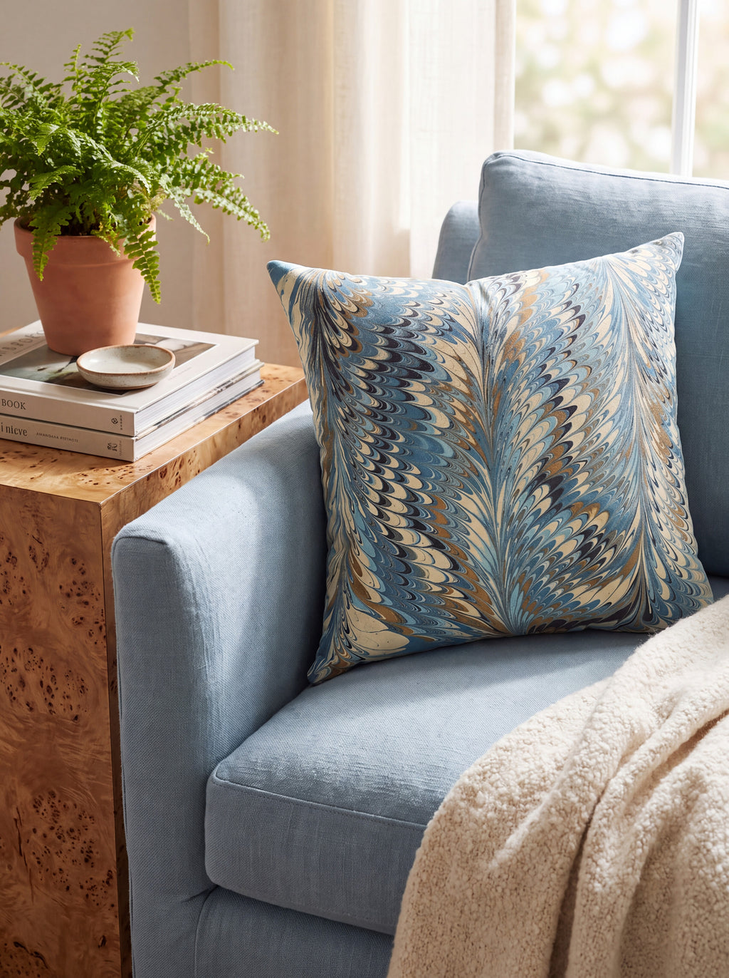 The Conway hand-marbled pillow cover in indigo and gold styled on a pale blue armchair