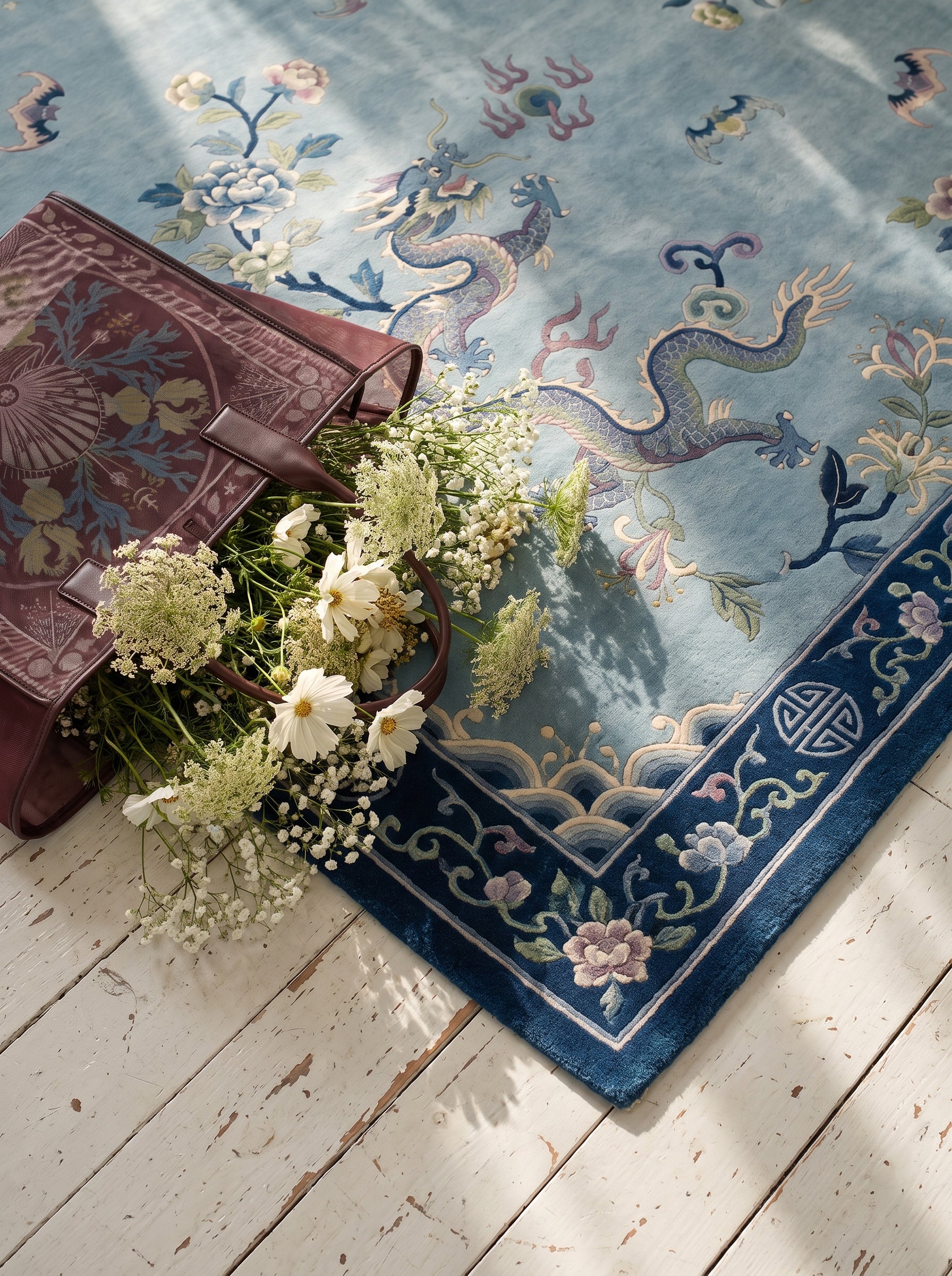 A light blue Chinese Art Deco area rug with dragons and floral borders, styled on a white wooden floor with white flowers.