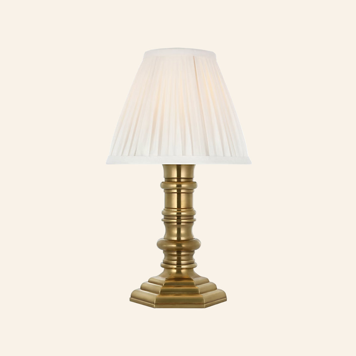 12-inch Ellis cordless candlestick lamp in natural brass with a turned column base, stepped octagonal foot and white pleated silk shade, by Kevin Francis Design