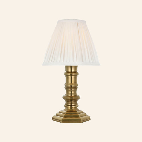 12-inch Ellis cordless candlestick lamp in natural brass with a turned column base, stepped octagonal foot and white pleated silk shade, by Kevin Francis Design