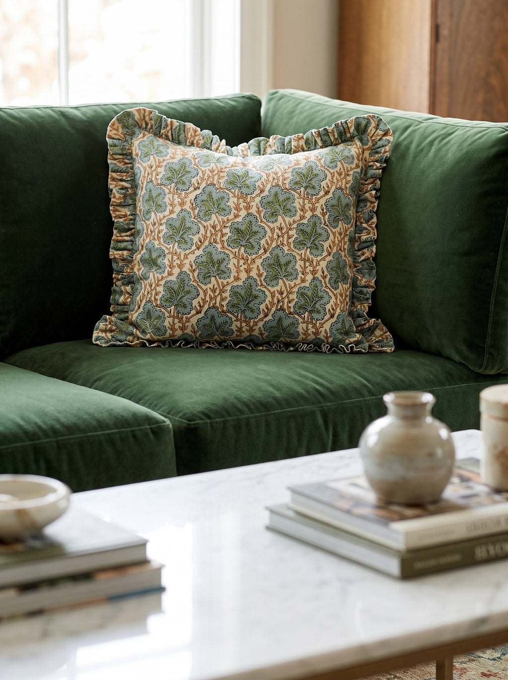 The Longleaf ruffled block print pillow cover in sage and teal styled on a green velvet sofa