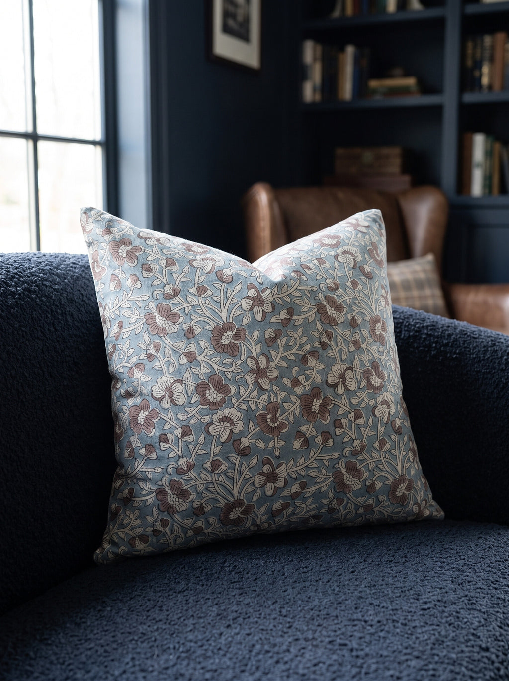 The Rilman block print pillow cover in light blue and brown styled on a navy boucle sofa