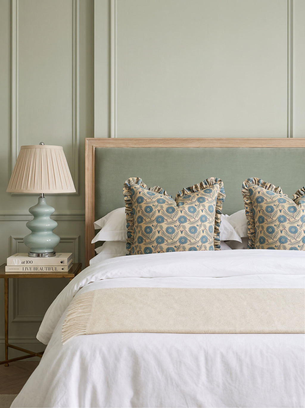 Waverly ruffled block print pillow covers in teal and blue styled on a bed with a sage upholstered headboard