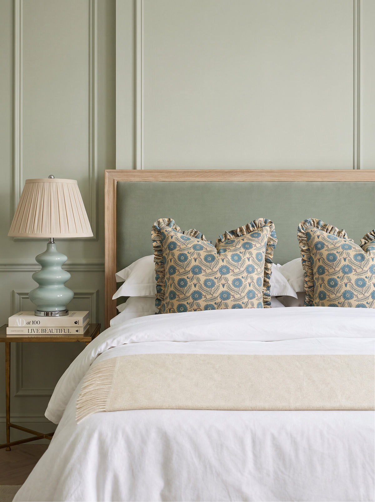 Waverly ruffled block print pillow covers in teal and blue styled on a bed with a sage upholstered headboard