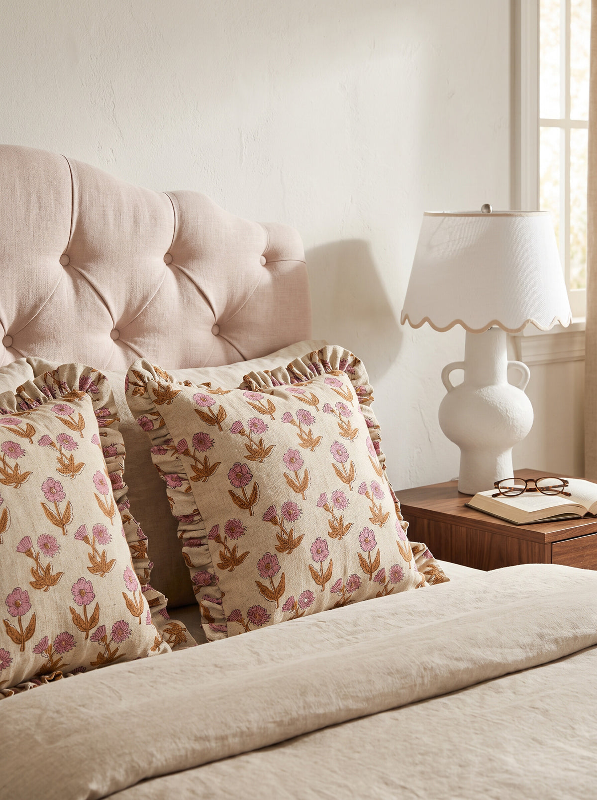 Wesley ruffled block print pillow covers in pink and mustard styled on a bed with a tufted blush headboard